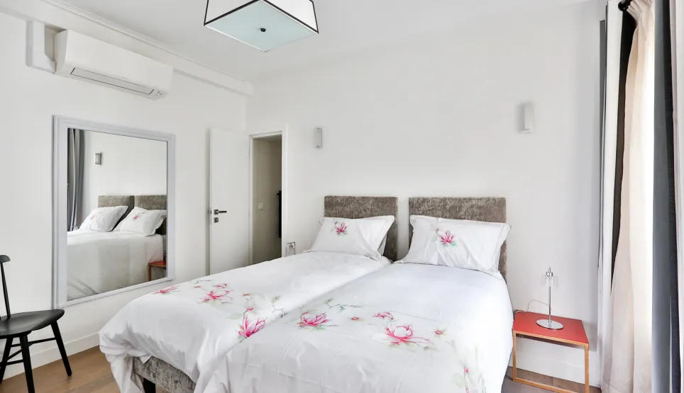 Élégante chambre moderne avec lits jumeaux, climatisation, miroir et décoration florale. Confort et design pour votre propriété de luxe.