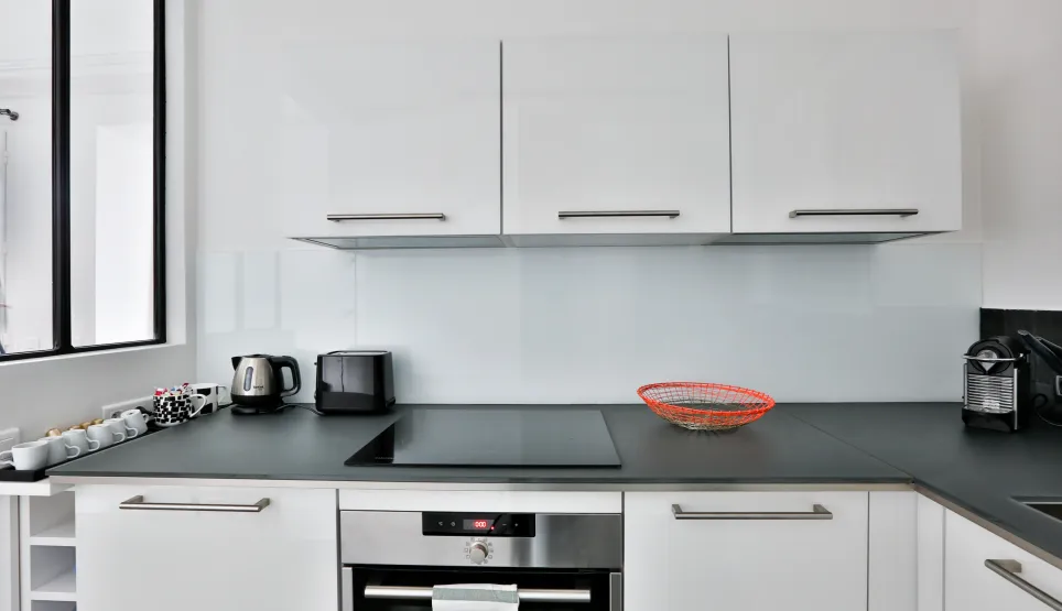 Cuisine moderne blanche et épurée avec électroménager intégré, plan de travail foncé. Idéal pour appartement de luxe.