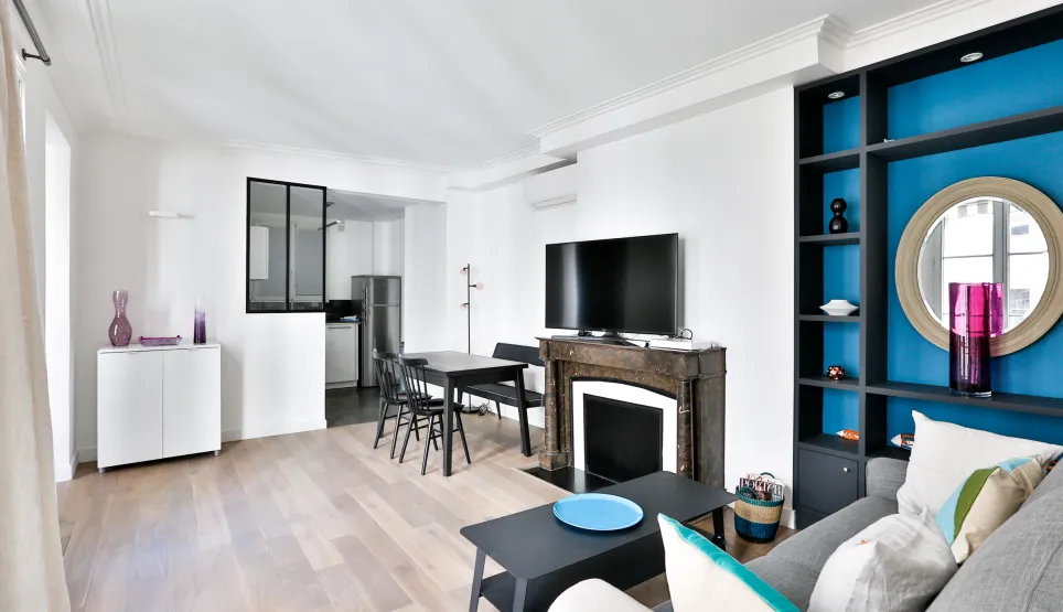 Salon moderne lumineux avec cuisine ouverte, cheminée, rangements intégrés bleus. Design contemporain pour appartement de luxe.