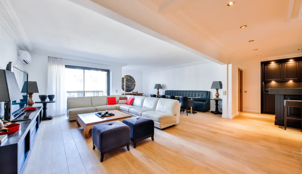 Salon de luxe spacieux et lumineux avec parquet clair, canapé sectionnel moderne, coin repas et bar intégré. Design contemporain haut de gamme.