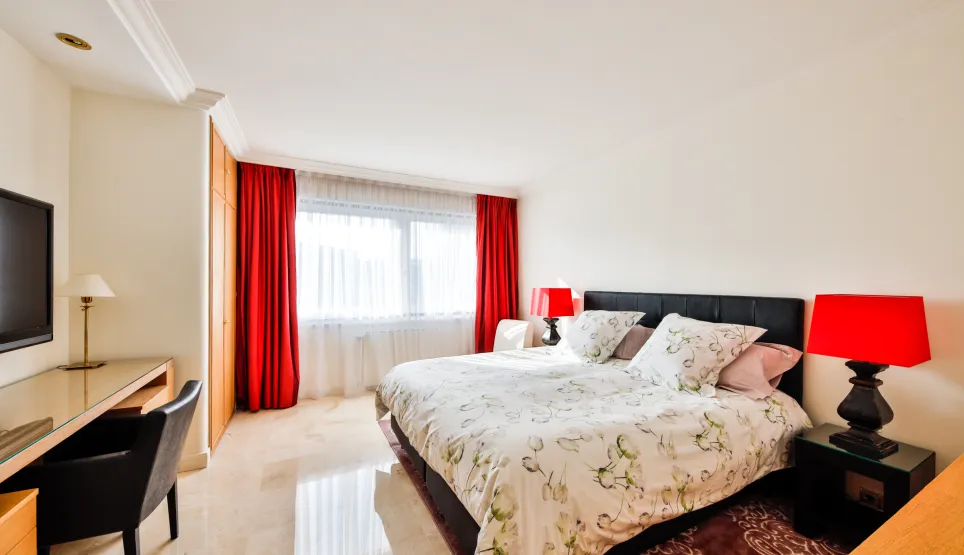 Splendide chambre de luxe avec lit king-size, rideaux rouges, sol en marbre, bureau et TV. Design moderne et lumineux.