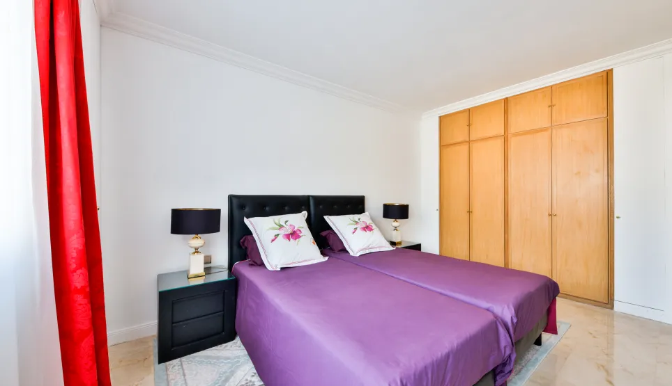 Chambre élégante avec lits jumeaux, literie violette, tables de chevet design et placards intégrés. Confort et style pour propriété de luxe.
