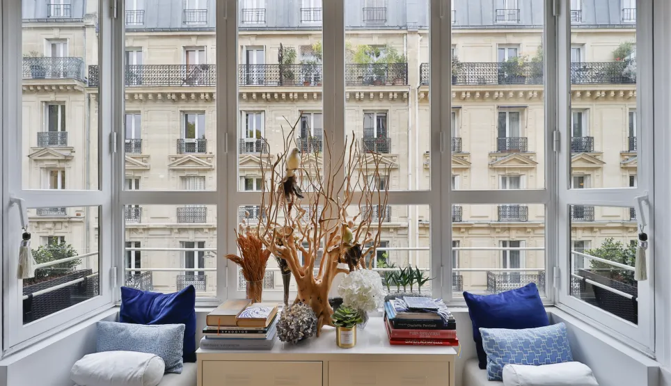 Appartement de luxe avec vue imprenable sur Paris. Fenêtre panoramique, coin lecture élégant, design intérieur raffiné. Lumière naturelle.