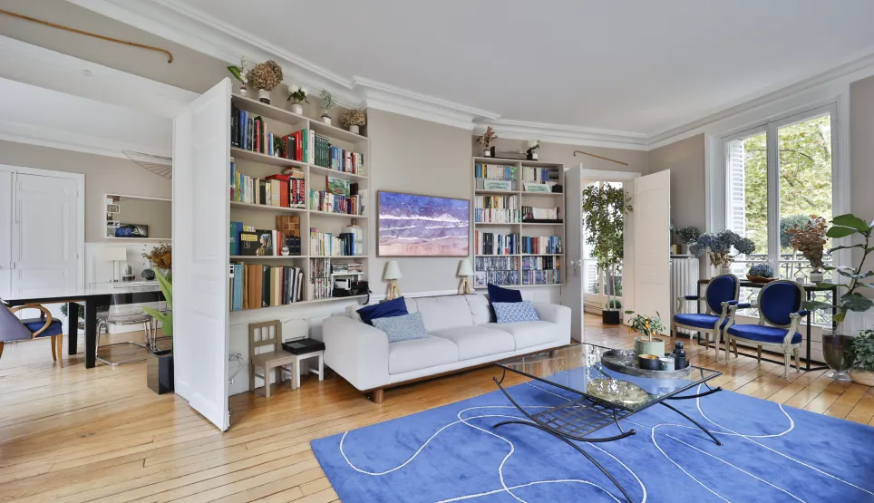 Vaste salon-séjour lumineux avec parquet, bibliothèque, canapé design, et vue verdoyante. Ambiance élégante et moderne pour un appartement de luxe.