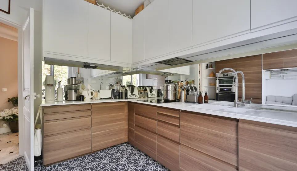 Cuisine de luxe moderne avec meubles bois et blanc, plan de travail épuré, électroménager intégré et carrelage design. Ambiance élégante et lumineuse.