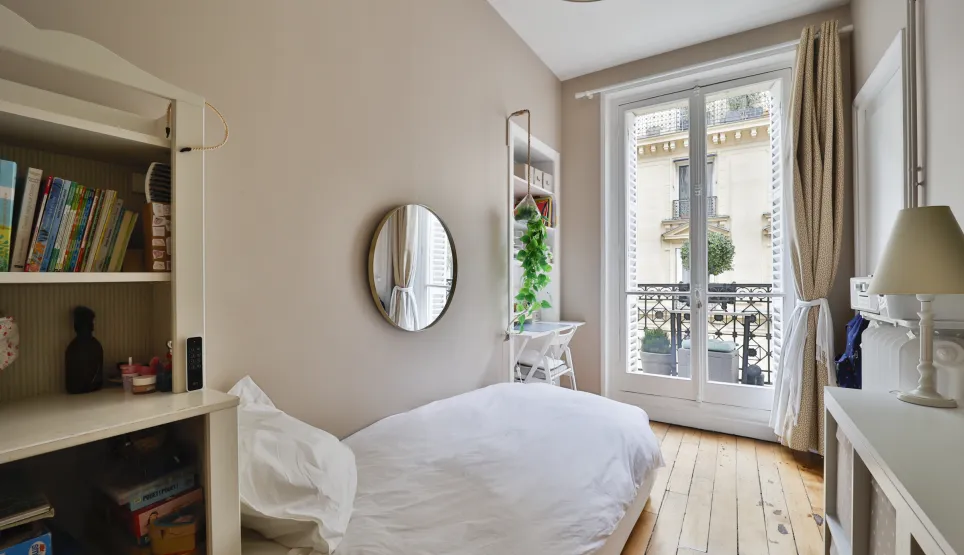 Chambre lumineuse avec balcon parisien, parquet et vue dégagée. Un espace cosy et élégant pour un appartement de charme.