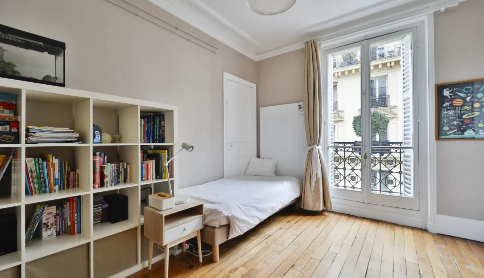 Chambre lumineuse avec parquet, fenêtre française et balcon. Design épuré, espace optimisé. Idéal pour un studio parisien de luxe.