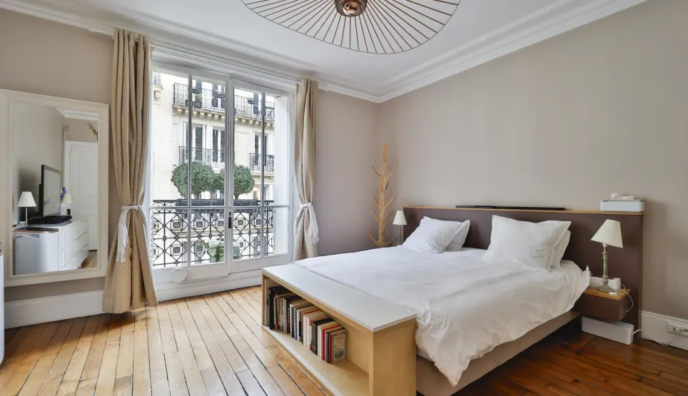Chambre de luxe parisienne lumineuse avec parquet, balcon, vue Haussmannienne. Design moderne et élégant pour un appartement d'exception.