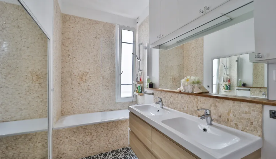 Salle de bain moderne et lumineuse avec double vasque, baignoire, carrelage élégant et miroir intégré. Design contemporain pour un confort optimal.