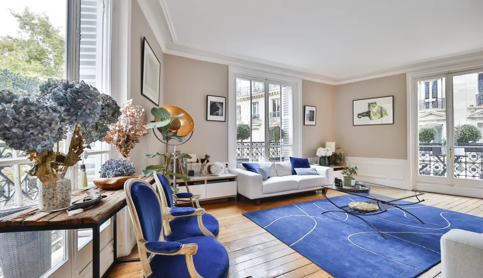 Salon de luxe parisien Haussmannien. Design raffiné, mobilier bleu élégant, parquet. Lumière naturelle, vue ville. Appartement prestige.
