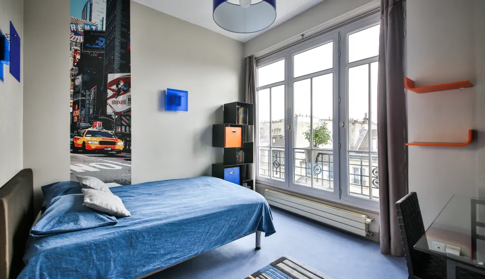 Chambre moderne et lumineuse d'un appartement de luxe. Lit confortable, vue ville, décoration urbaine chic avec fresque Times Square. Design contemporain.