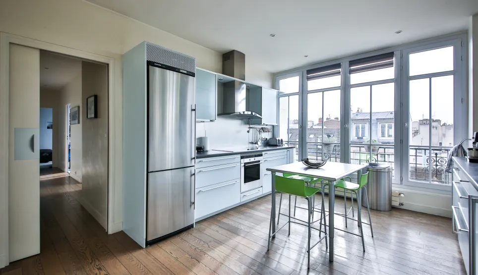 Cuisine design lumineuse, électroménager inox, parquet. Grandes baies vitrées avec vue ville. Appartement de luxe moderne et fonctionnel.