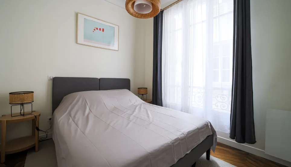 Chambre élégante et lumineuse avec lit double, décoration moderne et fenêtre offrant une belle lumière naturelle. Idéal pour un appartement de luxe.