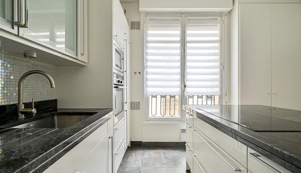 Cuisine de luxe moderne et lumineuse avec plans de travail en granit noir, équipements intégrés et grandes fenêtres. Idéal pour appartement de prestige.