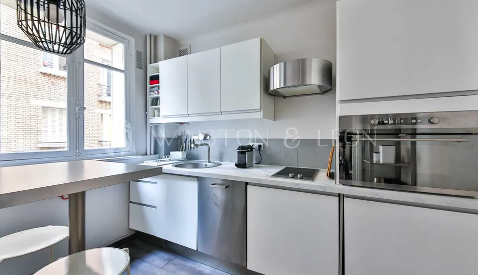 Cuisine moderne lumineuse, mobilier blanc épuré, électroménager inox intégré, coin repas. Design contemporain idéal pour appartement de luxe.