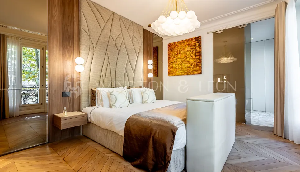 Chambre de luxe moderne avec tête de lit capitonnée, parquet chevron, éclairage design et touches artistiques. Élégance parisienne.