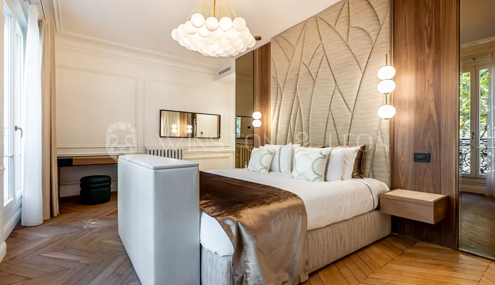Chambre luxueuse au design contemporain et classique. Tête de lit texturée, parquet élégant, éclairage sophistiqué. Idéal pour immobilier haut de gamme.