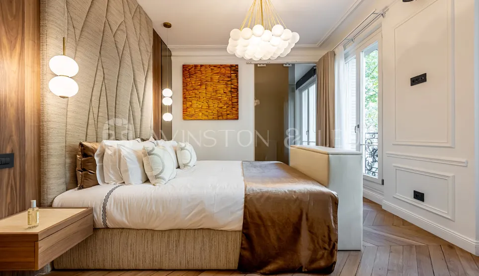 Chambre de luxe parisienne, design moderne, tête de lit texturée, parquet, éclairage élégant. Confort et style pour un appartement d'exception.