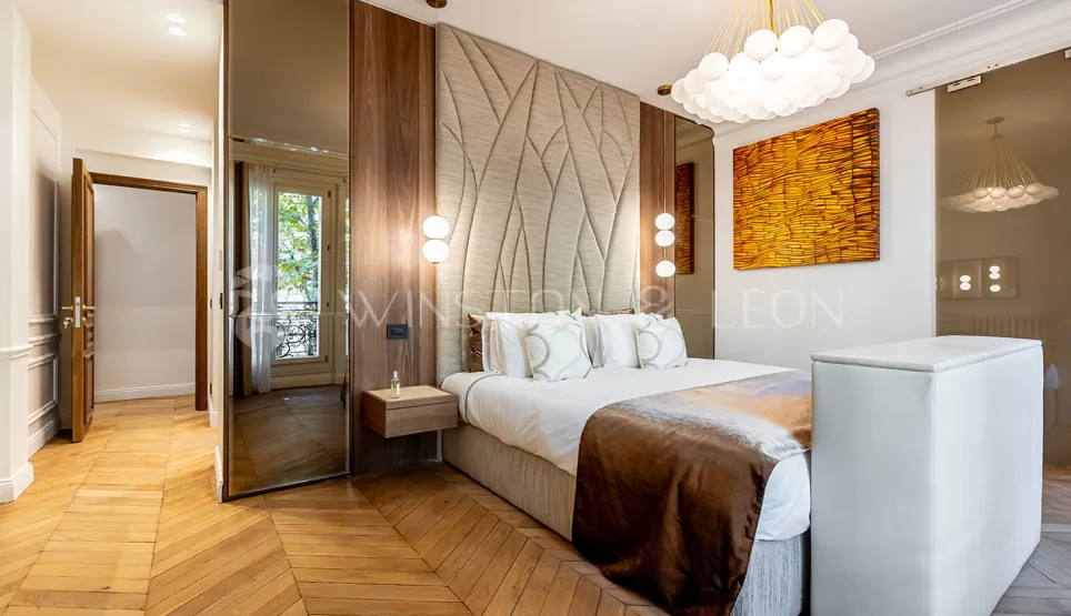 Chambre parentale luxe moderne: tête de lit design, parquet chevron, boiseries élégantes, éclairage contemporain. Ambiance raffinée et confort premium.