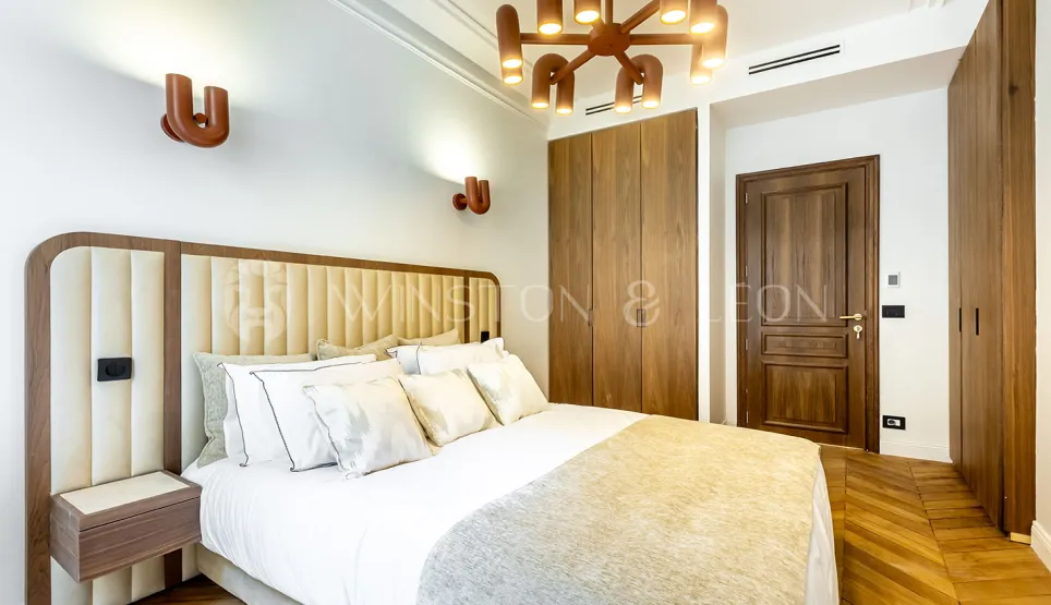 Chambre de luxe moderne avec tête de lit capitonnée, éclairage design, dressing intégré et parquet. Élégance et confort.
