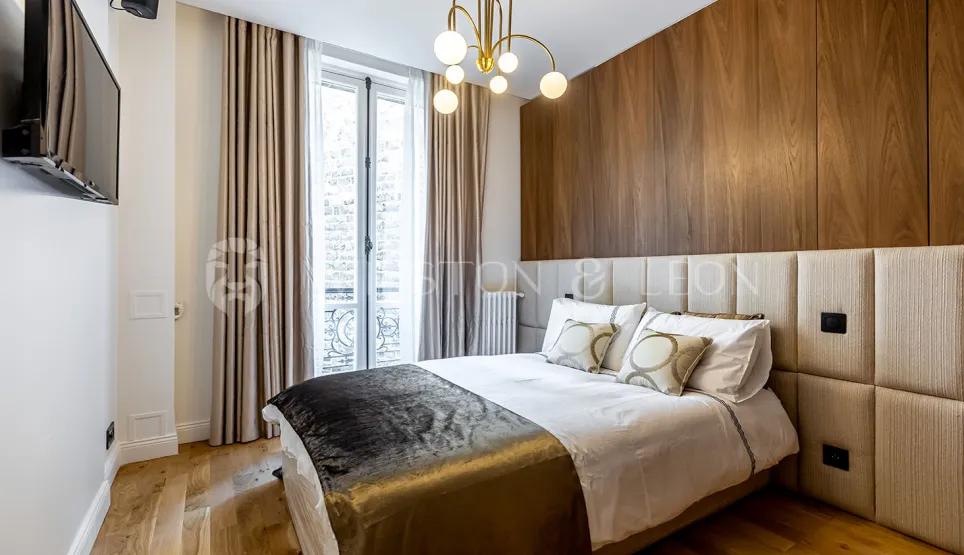 Chambre de luxe moderne avec boiseries murales, tête de lit rembourrée et lustre élégant. Confort et design contemporain pour un appartement parisien.