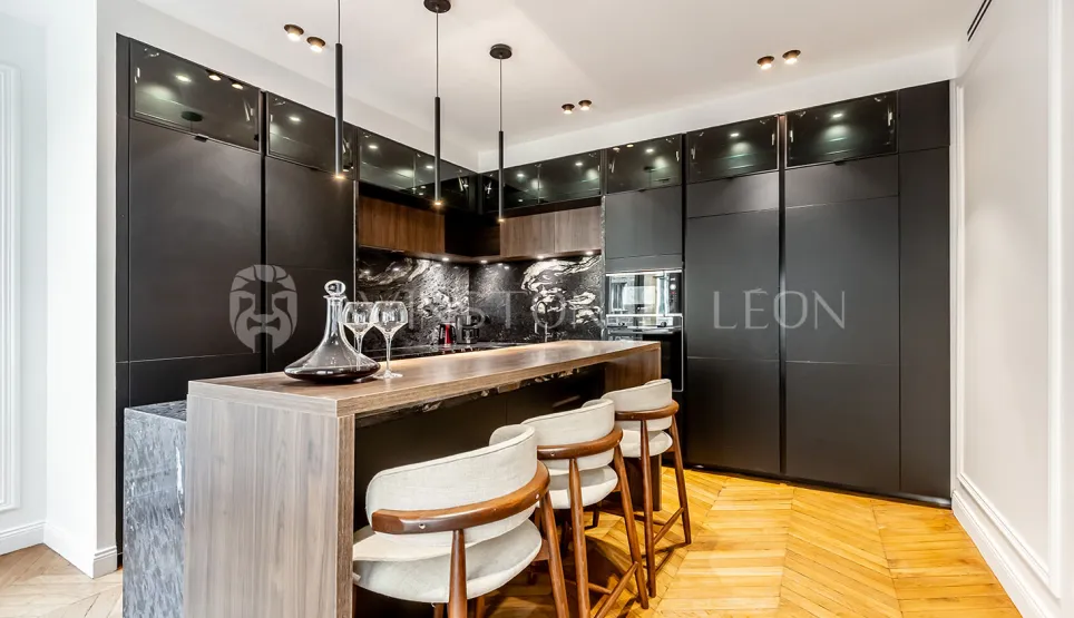 Cuisine de luxe contemporaine avec îlot bar, finitions noires mates, bois clair, marbre et parquet. Élégance et fonctionnalité.