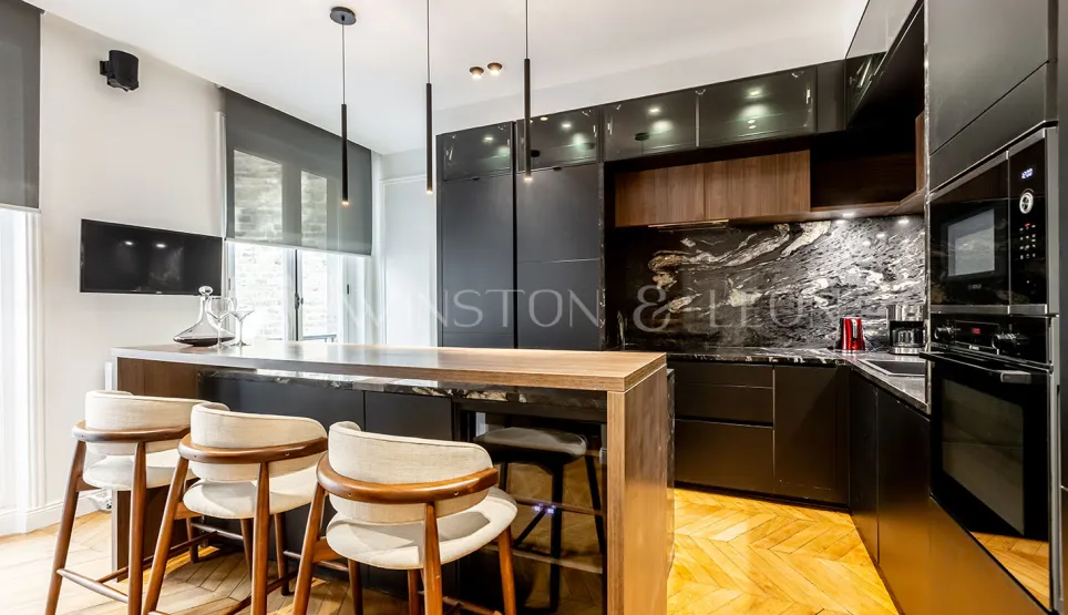 Cuisine luxe moderne avec îlot bois, marbre noir veiné, tabourets design et luminaires suspendus.