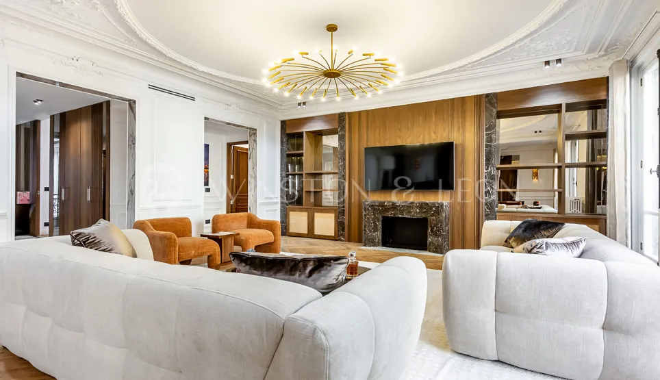 Salon de luxe contemporain avec cheminée marbre, TV intégrée, canapés blancs et lustre doré. Design intérieur élégant pour appartement prestige.