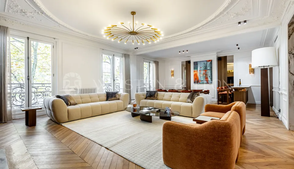 Grand salon de luxe haussmannien. Design contemporain, parquet chevrons, moulures élégantes et lustre moderne. Appartement de prestige.