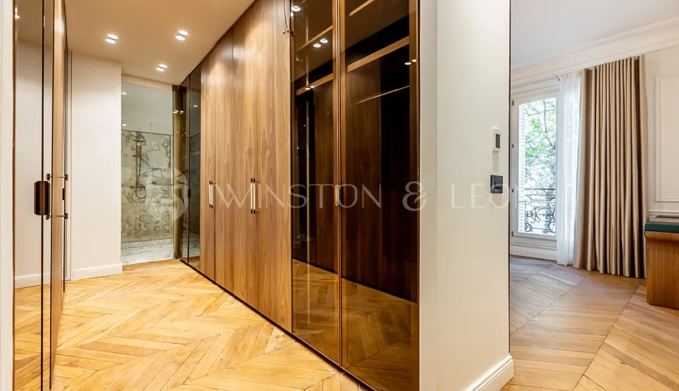 Luxueux dressing sur mesure en bois et verre, parquet chevron. Salle de bain attenante. Design élégant pour un appartement de prestige.