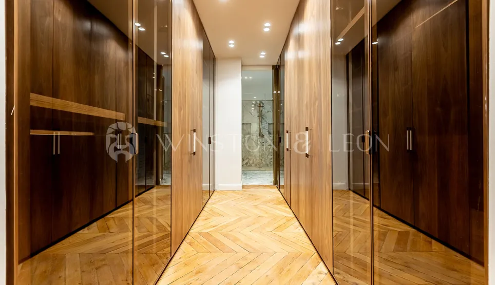 Dressing de luxe moderne avec placards en bois et verre, parquet chevrons. Rangement élégant pour propriété haut de gamme.