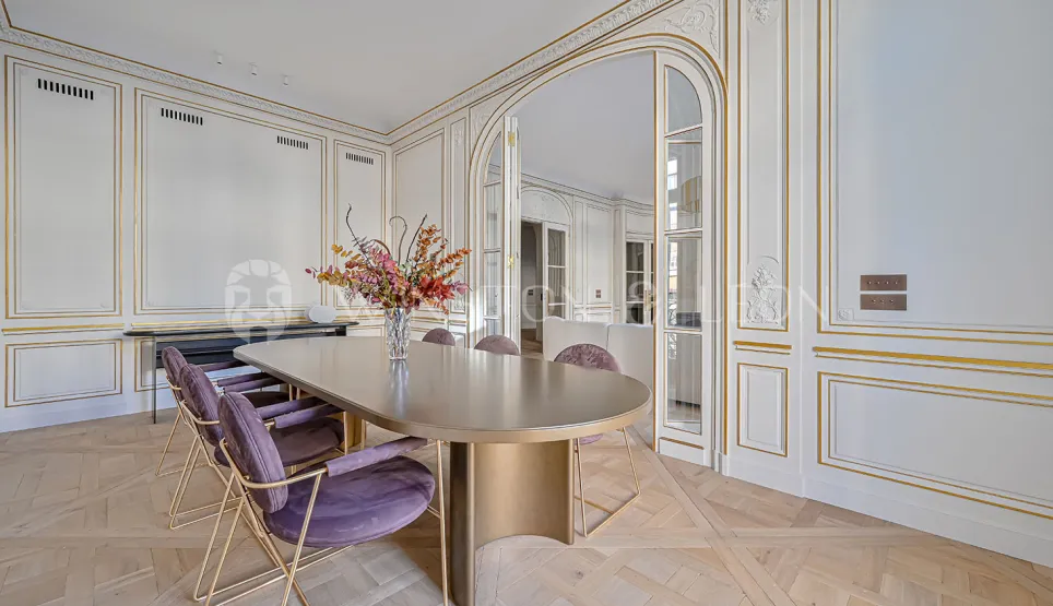 Élégante salle à manger de luxe parisienne. Boiseries dorées, parquet, table design moderne, chaises velours. Raffinement Haussmannien.