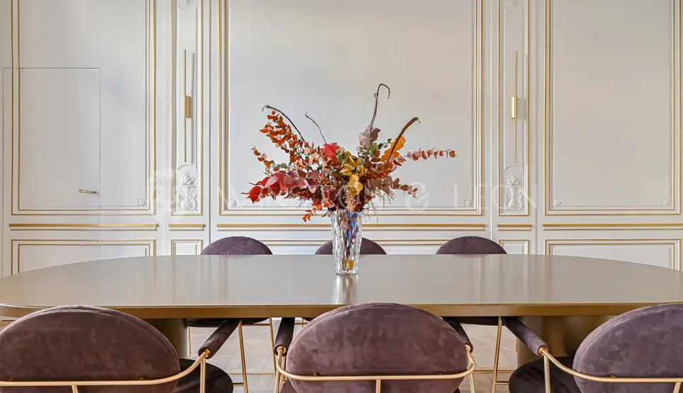 Appartement haussmannien de luxe: salle à manger élégante. Moulures dorées, mobilier contemporain velours et table design. Décoration raffinée.