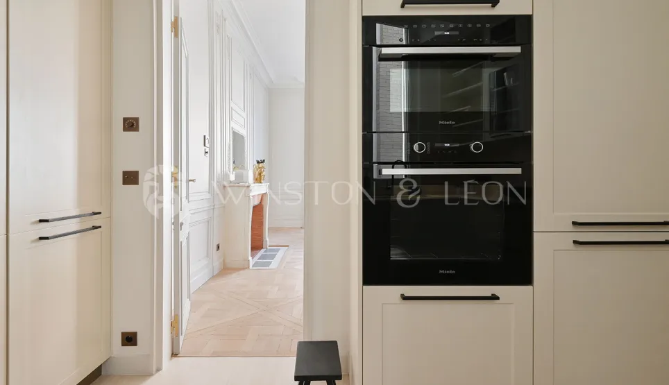 Cuisine Miele moderne et élégante, ouvrant sur un salon Haussmannien. Appartement de luxe rénové à Paris.