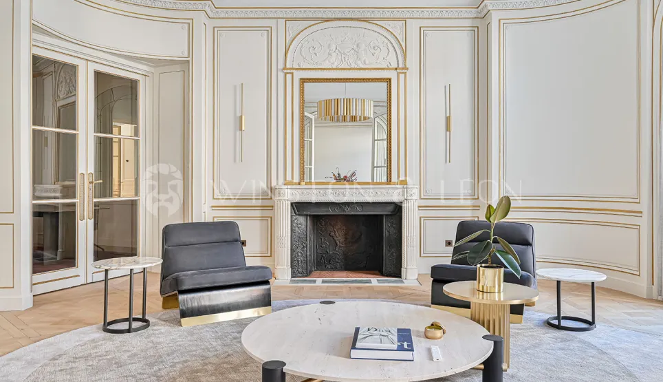 Appartement de luxe parisien, salon Haussmannien raffiné avec boiseries dorées, cheminée marbre et mobilier contemporain chic.