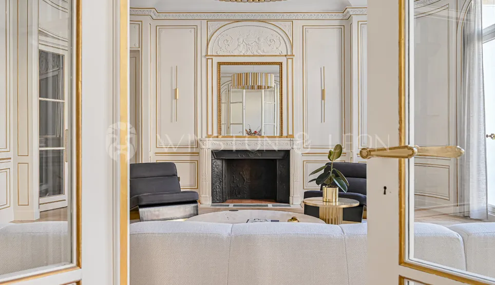 Salon de luxe parisien avec moulures dorées, cheminée classique et mobilier élégant. Un intérieur prestigieux alliant charme ancien et design moderne.