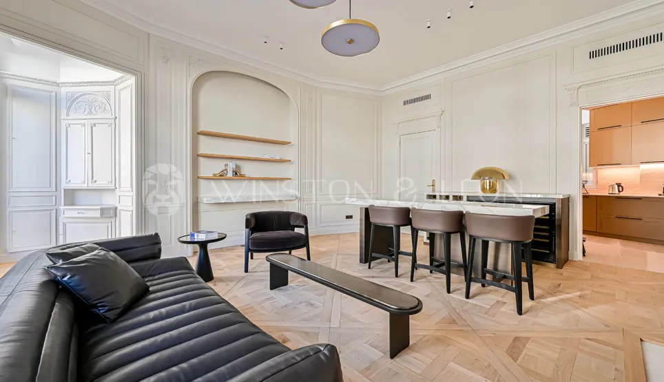 Superbe salon de luxe parisien. Design contemporain, parquet Versailles, moulures élégantes, bar intégré et cuisine moderne. Ambiance raffinée et lumineuse.