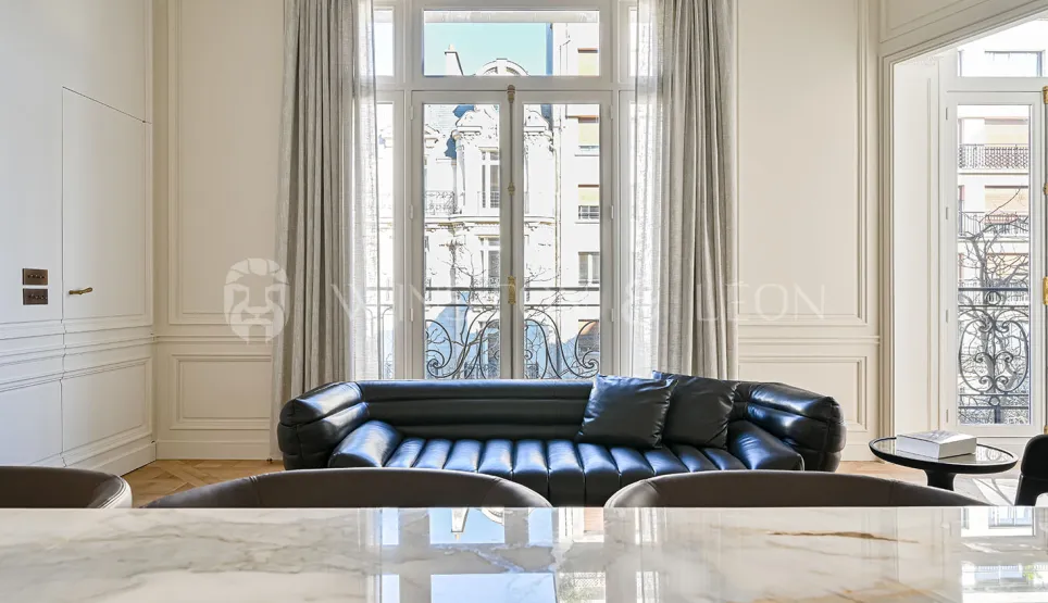 Salon de luxe parisien avec canapé cuir noir, moulures élégantes et vue haussmannienne. Design contemporain et raffinement.