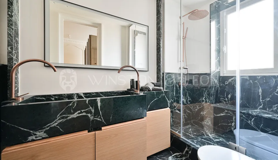 Salle de bain de luxe. Marbre noir veiné blanc, double vasque bois clair, robinetterie cuivre. Douche italienne moderne. Élégance et raffinement.