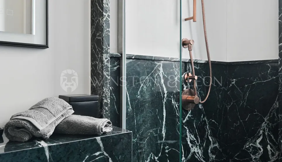 Salle de bain de luxe avec marbre vert veiné et robinetterie cuivre. Douche élégante, design contemporain. Idéal pour immobilier haut de gamme.
