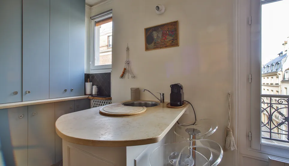 Cuisine moderne et élégante avec îlot/bar, vue imprenable sur les toits de Paris. Appartement de luxe parisien, design contemporain.