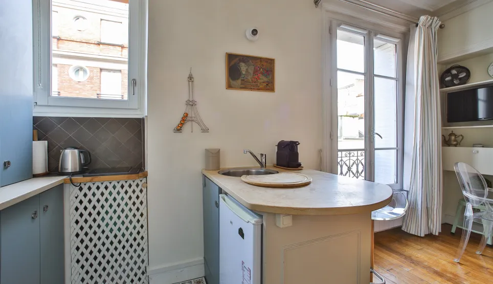 Photo d'un studio parisien optimisé avec cuisine intégrée, fenêtre lumineuse, parquet et décor Tour Eiffel. Ambiance chic et fonctionnelle.