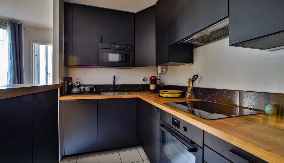 Cuisine haut de gamme, mobilier noir mat, plan de travail bois. Électroménager intégré. Ambiance moderne et luxueuse.