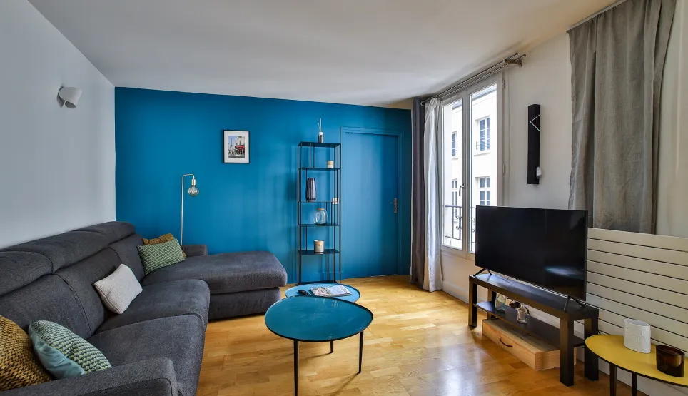 Salon moderne et lumineux avec mur bleu vibrant, canapé d'angle gris, parquet élégant. Idéal pour un appartement de luxe au design contemporain.