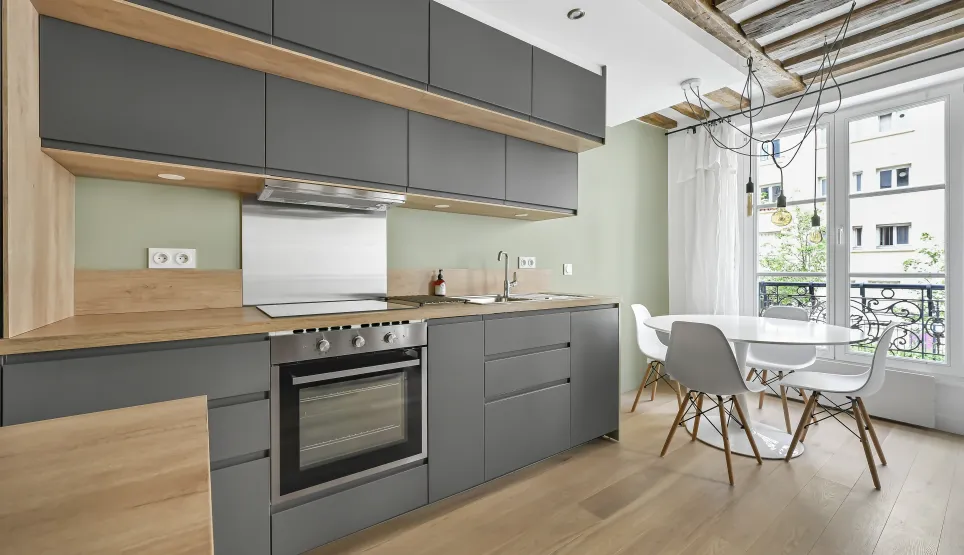 Cuisine moderne gris anthracite et bois clair. Design épuré, poutres apparentes, vue ville. Appartement de luxe lumineux.