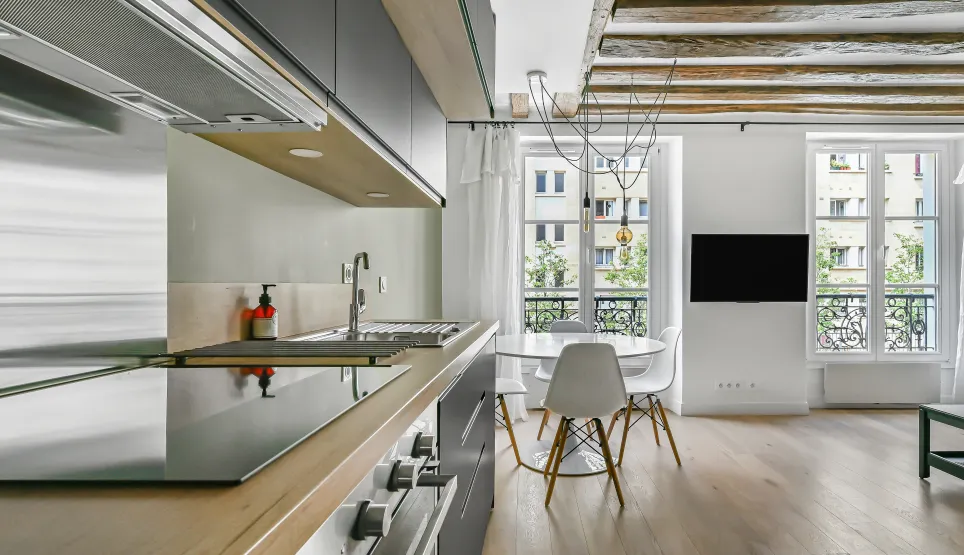 Appartement de luxe: cuisine moderne ouverte sur séjour lumineux, poutres apparentes, parquet. Élégance parisienne.
