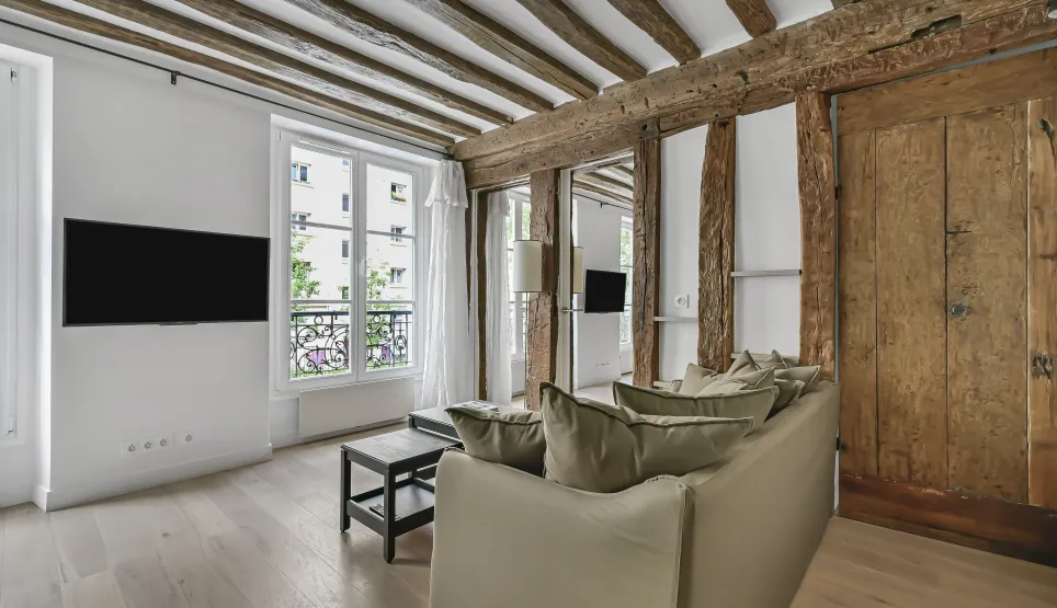 Salon lumineux d'appartement de luxe parisien avec poutres apparentes, parquet clair et touches modernes. Charme et élégance.
