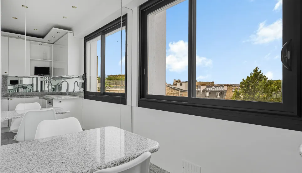 Cuisine moderne lumineuse, îlot en granit, vue urbaine. Design épuré pour un appartement de luxe contemporain.