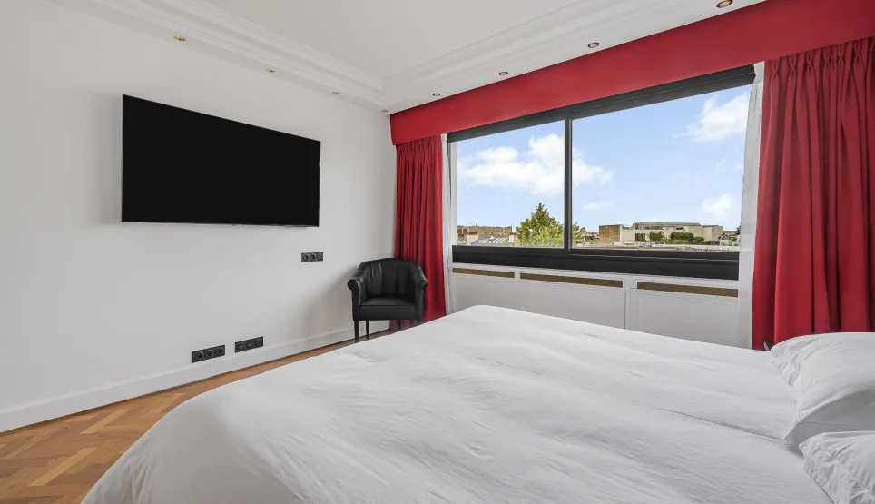 Suite parentale moderne et lumineuse avec vue citadine, TV, fauteuil et parquet. Le luxe et le confort d'un appartement haut de gamme.