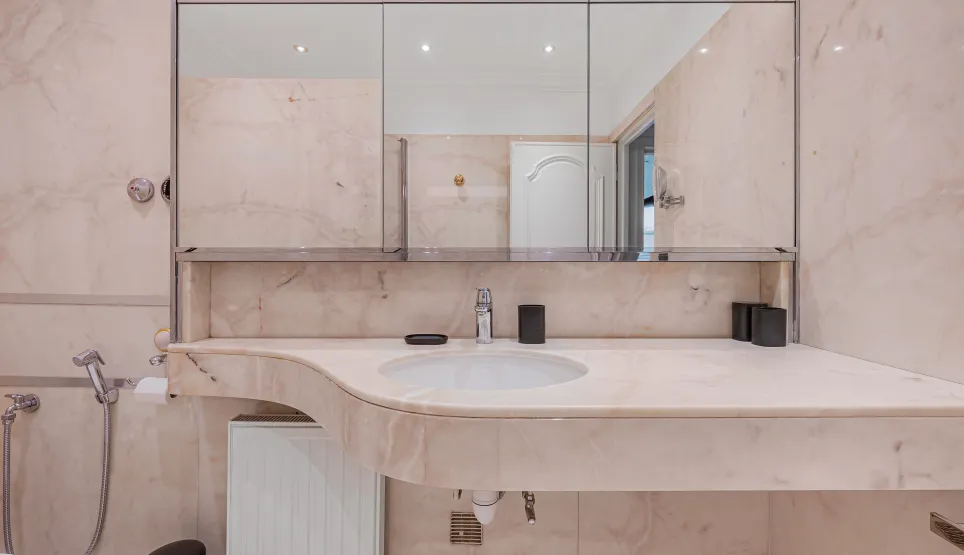 Salle de bain luxueuse en marbre clair, lavabo design et miroir. Ambiance raffinée pour une propriété d'exception.